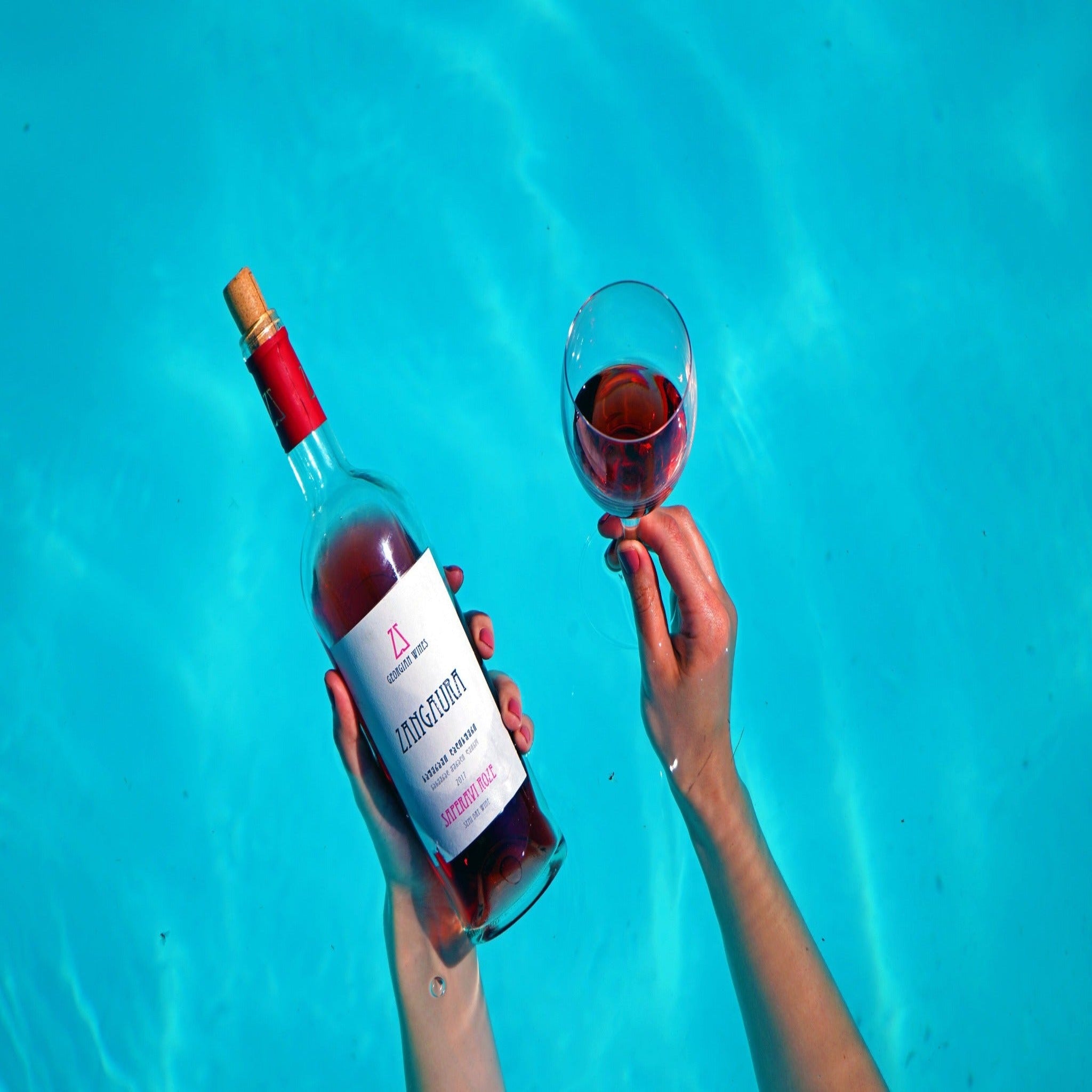 a female hand holding rose bottle in the pool 